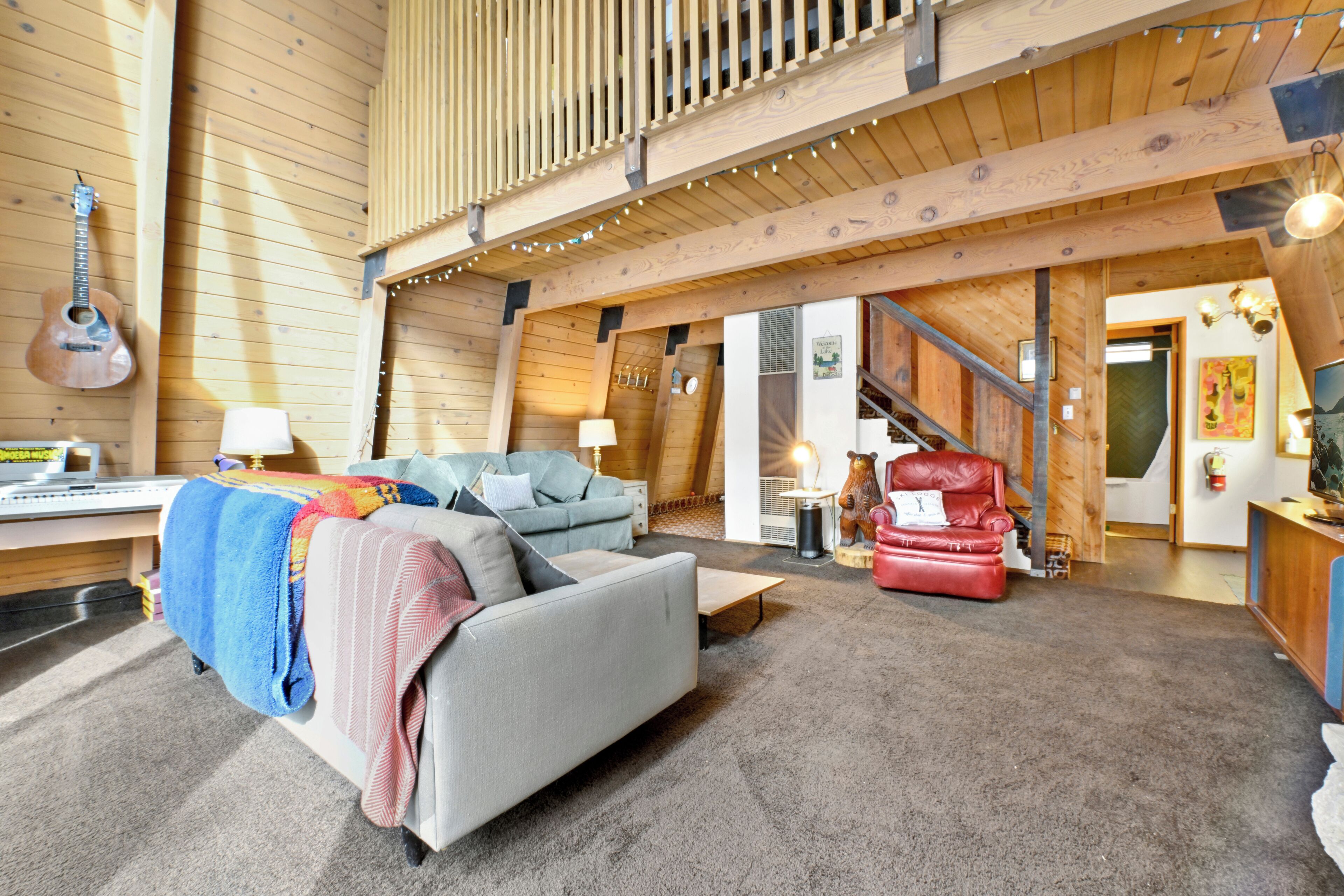 A cozy living room with a sofa, a red chair, a guitar, and a staircase leading to another room.