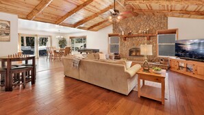 A spacious living room with a stone fireplace, wooden ceiling beams, and a large television. - Three Bears INN #2147 (Big Bear City)