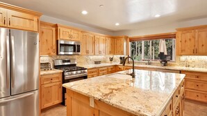 A modern kitchen with wooden cabinets, stainless steel appliances, granite countertops, and a large window providing a view of the outdoors. - Three Bears INN #2147 (Big Bear City)