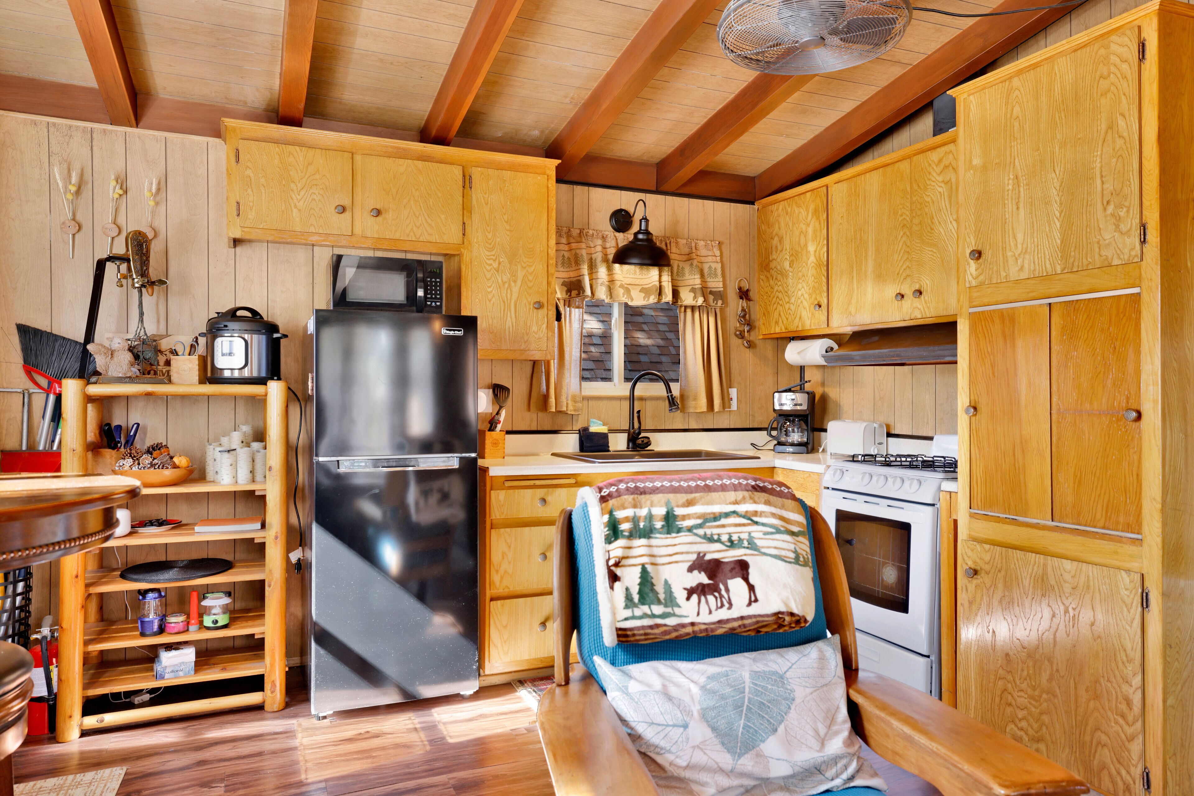 Cocina compacta con armarios de madera, refrigerador, microondas, estufa y un rincón de comedor con banco.
