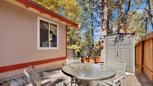 A patio with a round table and metal chairs, a wooden fence, and a shed in a backyard. - SKI View Chalet #2215 (Big Bear Lake)