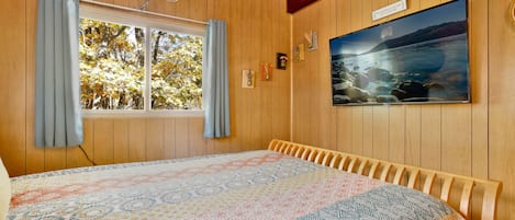A room with wooden paneling, a bed with a patterned bedspread, a window with curtains, and a framed picture on the wall.