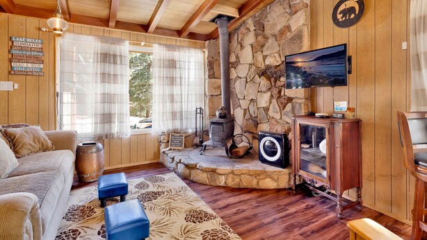 A cozy living room with a stone fireplace, a television, and a rustic wooden ceiling. - SKI View Chalet #2215 (Big Bear Lake)