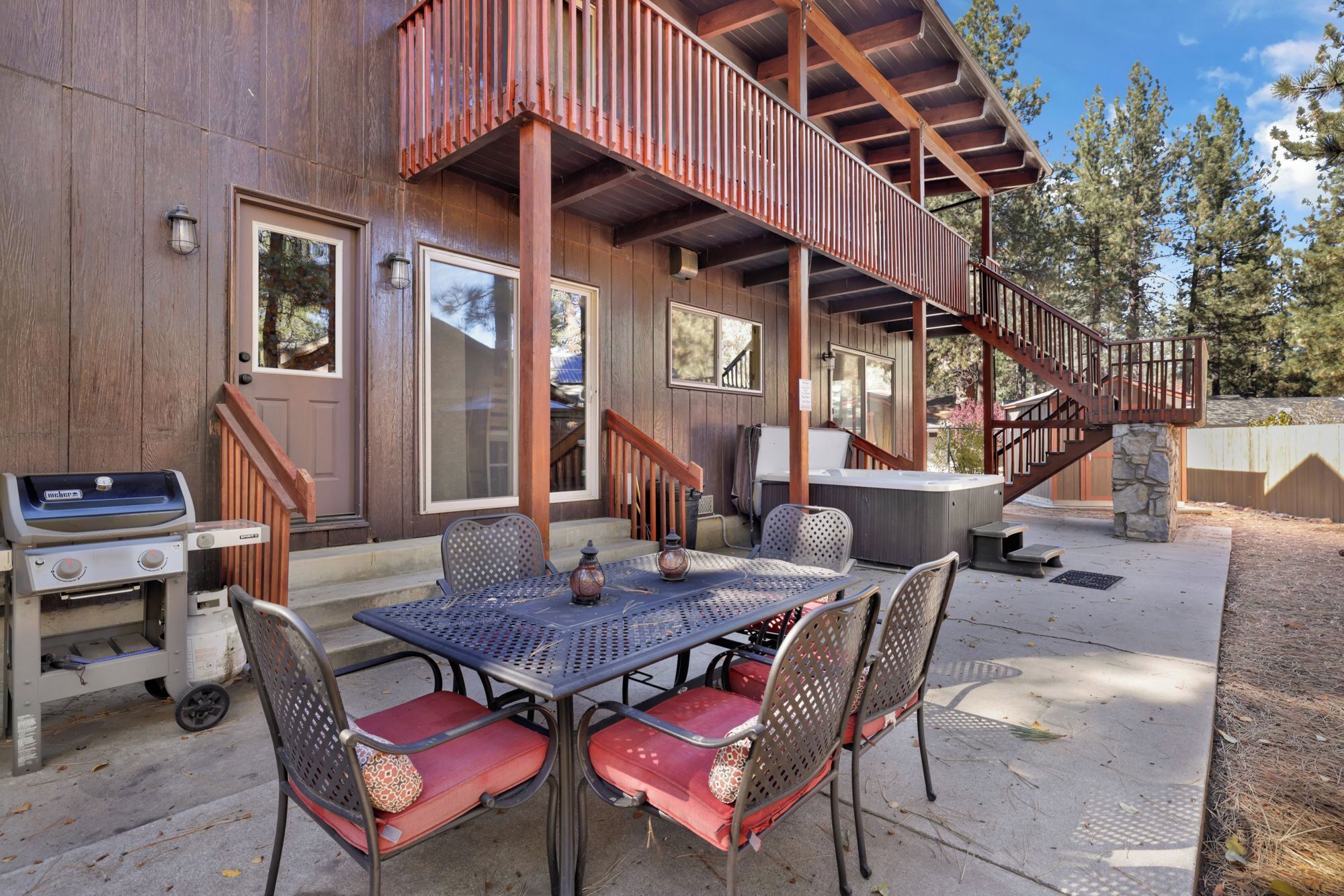 A wooden cabin with a deck, outdoor seating, a hot tub, and a grill.