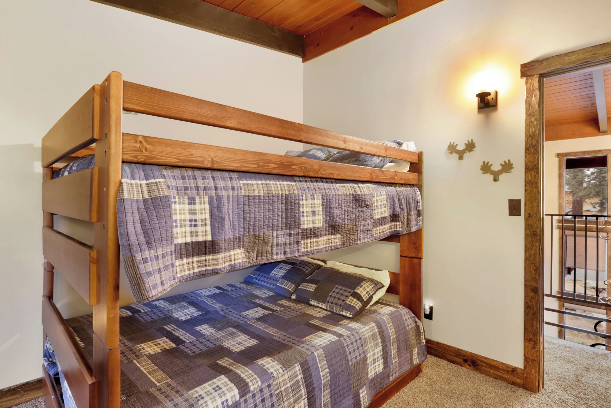 A bunk bed with a plaid quilt, wooden headboard, and a wall-mounted light fixture.