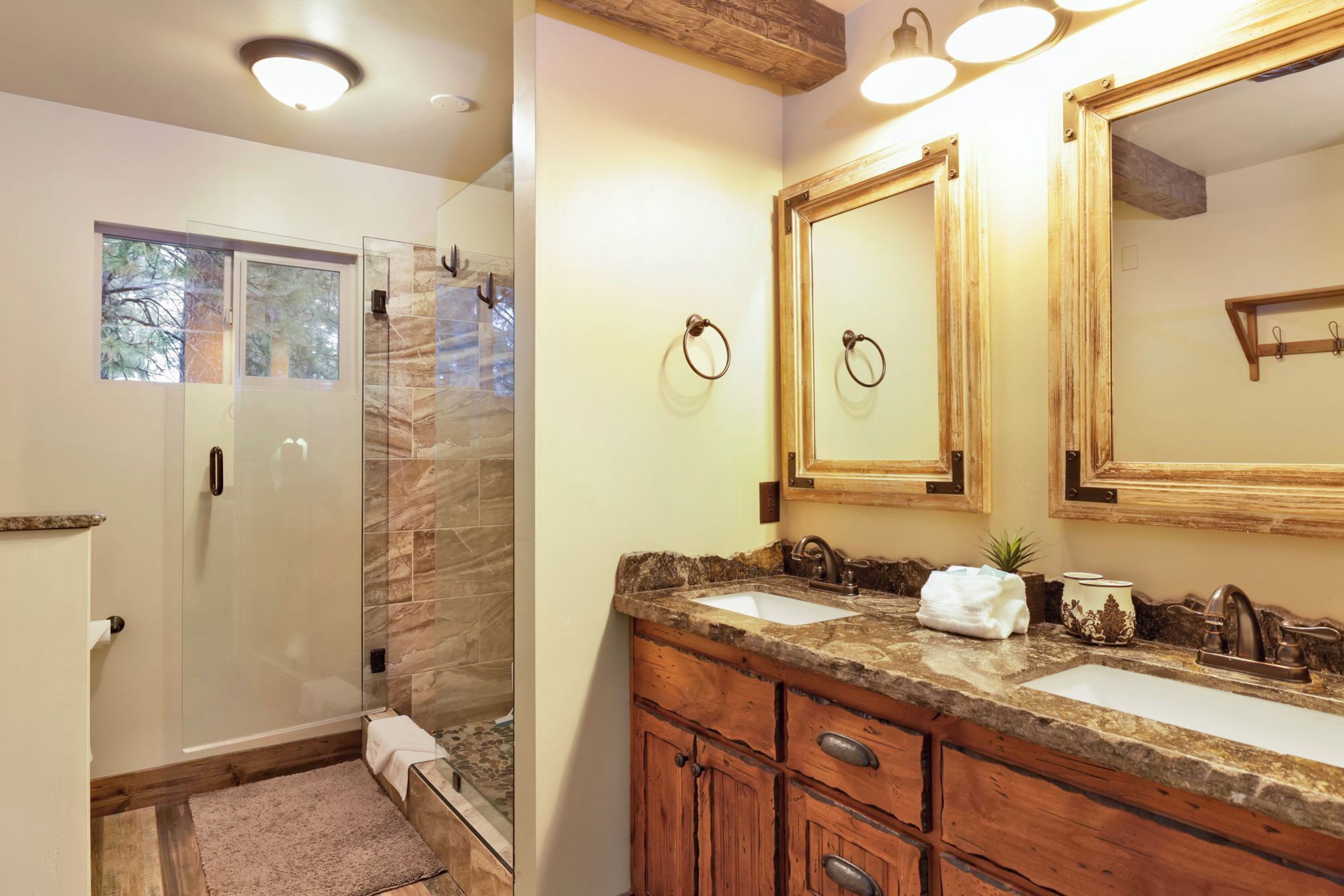 A bathroom with a glass shower enclosure, a vanity with a granite countertop, and a large mirror.