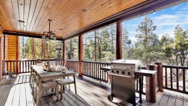 A wooden deck with a grill and dining table, surrounded by tall trees. - Gold Rush Lodge #2352 (Big Bear Lake)