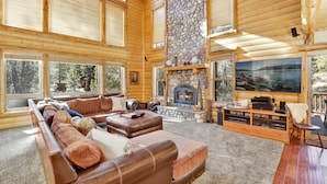 A log cabin interior with a stone fireplace, leather sofas, and a large TV screen. - Gold Rush Lodge #2352 (Big Bear Lake)
