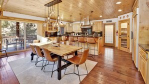 A spacious kitchen with wooden cabinets, a large dining table, and hanging pendant lights. - Gold Rush Lodge #2352 (Big Bear Lake)