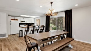 A modern kitchen with white cabinets, a wooden dining table with benches, and a chandelier.
