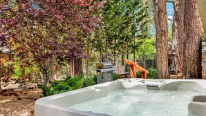 A hot tub in a garden with a grill and a wooden bench.