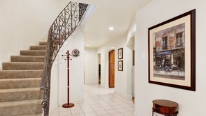 Un escalier avec une rampe en fer forgé, un porte-manteau et un tableau encadré au mur.