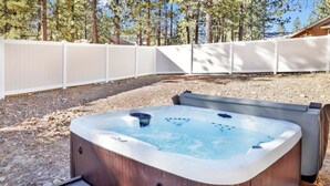 Un jacuzzi dans un jardin, avec une terrasse en bois et une clôture blanche.