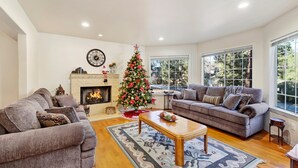 Un salon avec deux canapés, une table basse, une cheminée, un sapin de Noël et de grandes fenêtres.