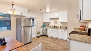 Eine moderne Küche mit weißen Schränken, einem Edelstahlkühlschrank, einer Granit-Arbeitsplatte und einem Holzessttisch.