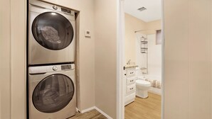 Ein Waschraum mit zwei übereinander gestapelten Waschmaschinen und ein Badezimmer mit Toilette und Spiegel.
