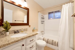 A bathroom with a granite countertop sink, a white toilet, a shower with a white curtain, and a large mirror with a wooden frame. - Robinhood Chalet #2277 (Big Bear City)