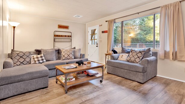 Ein modernes Wohnzimmer mit zwei grauen Sofas, einem Holztisch und einem großen Fenster mit Vorhängen.