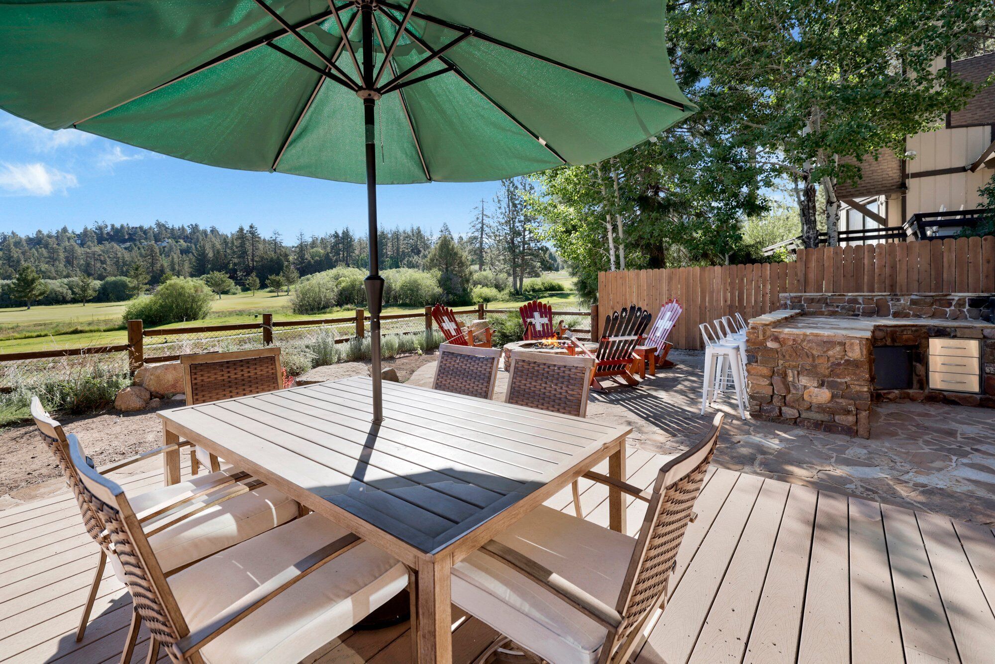 An outdoor patio with a wooden table and chairs, a stone fire pit, and a large green umbrella.