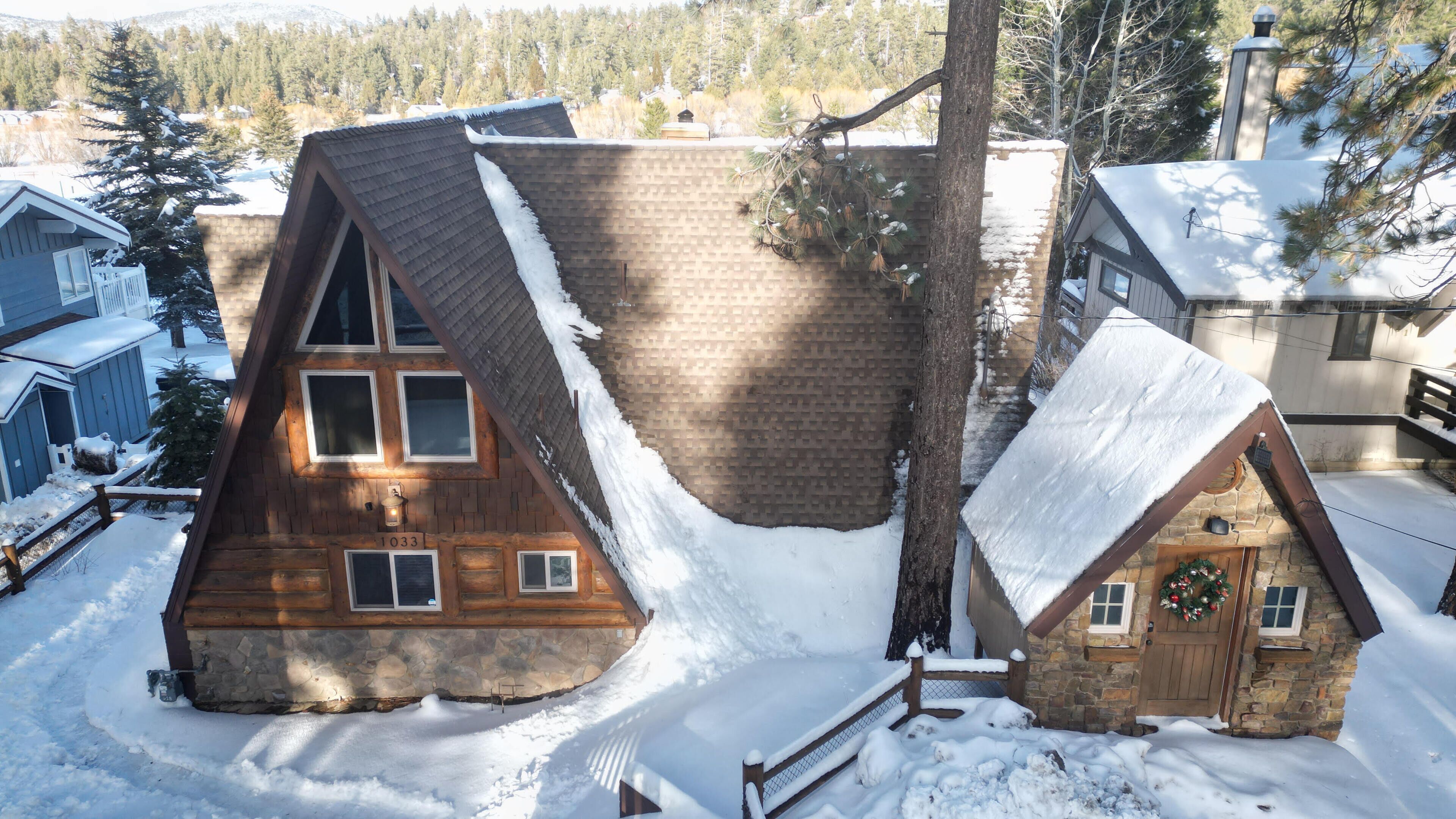 A wooden cabin with a steeply pitched roof, a stone chimney, and a snow-covered landscape.