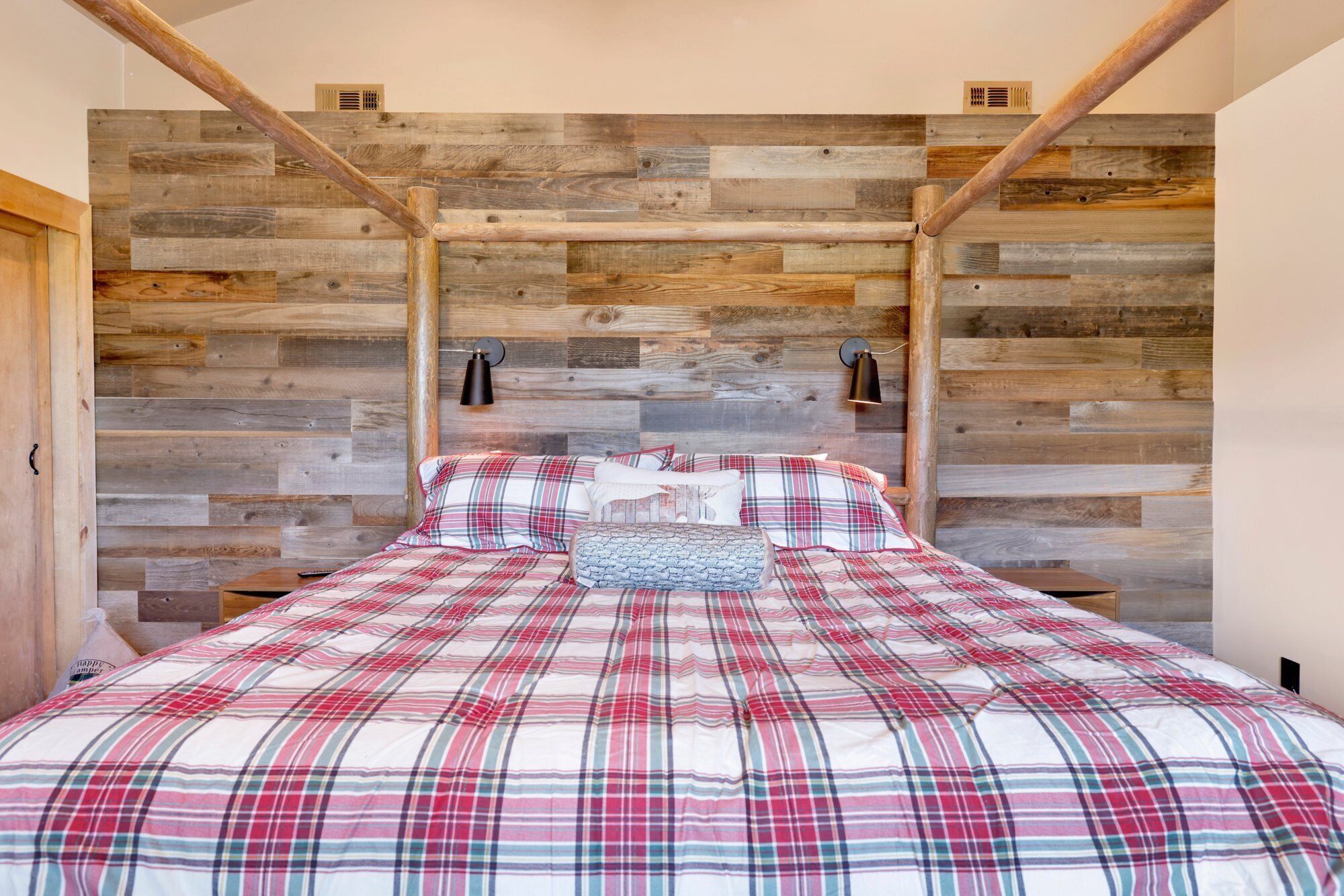 Een slaapkamer met een houten hoofdbord, ruitjes beddengoed en twee wandlampen.