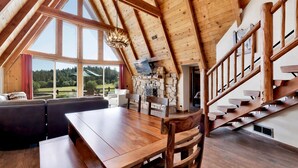 Ruime loft-achtige kamer met houten plafond, een stenen openhaard, een eettafel en een trap.
