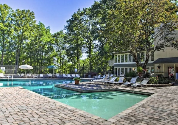 A swimming pool with lounge chairs and umbrellas, surrounded by trees and a building.