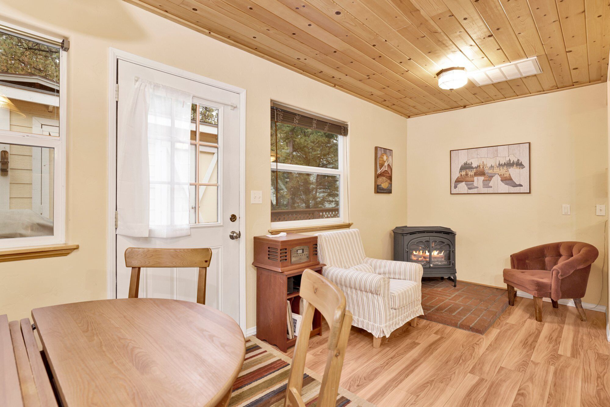 A cozy living room with a wooden ceiling, a fireplace, a striped armchair, and a dining table.