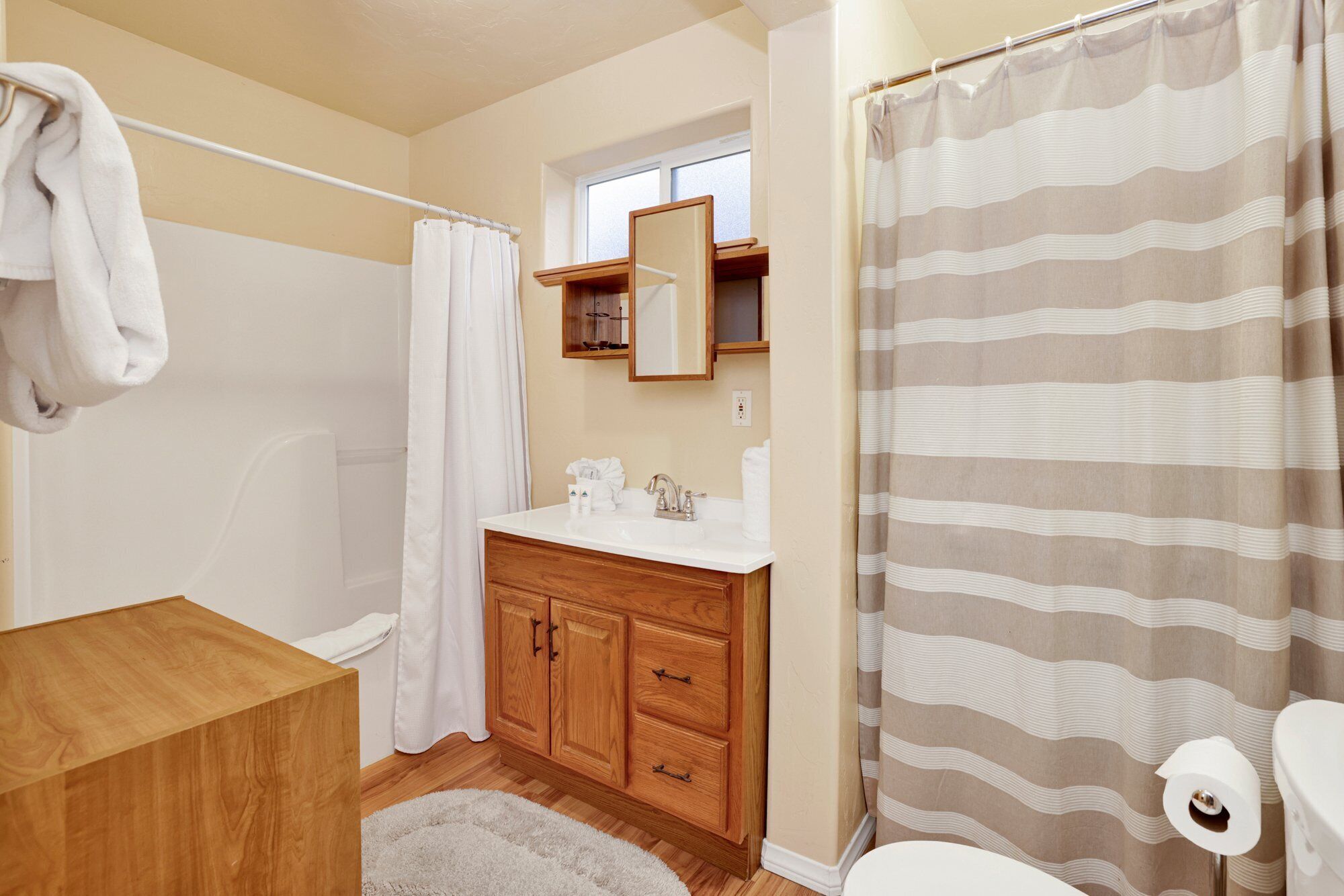 A bathroom with a wooden vanity, a white sink, a mirror above the sink, a shower curtain, and a toilet.