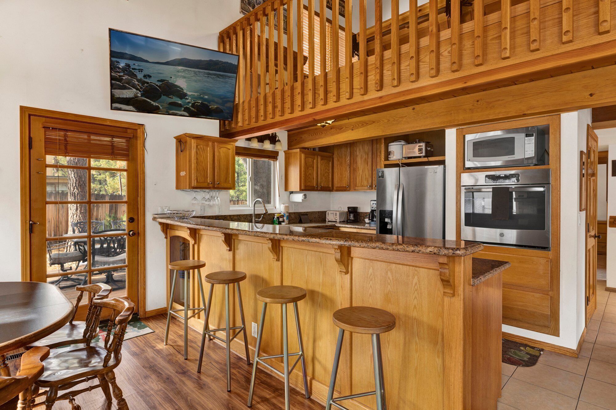 Una cocina con armarios de madera, encimera de granito, electrodomésticos de acero inoxidable y una barra de madera con taburetes.