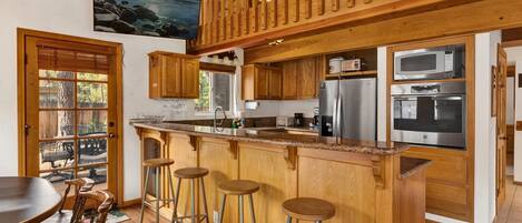 Una cocina con armarios de madera, encimera de granito, electrodomésticos de acero inoxidable y una barra de madera con taburetes.