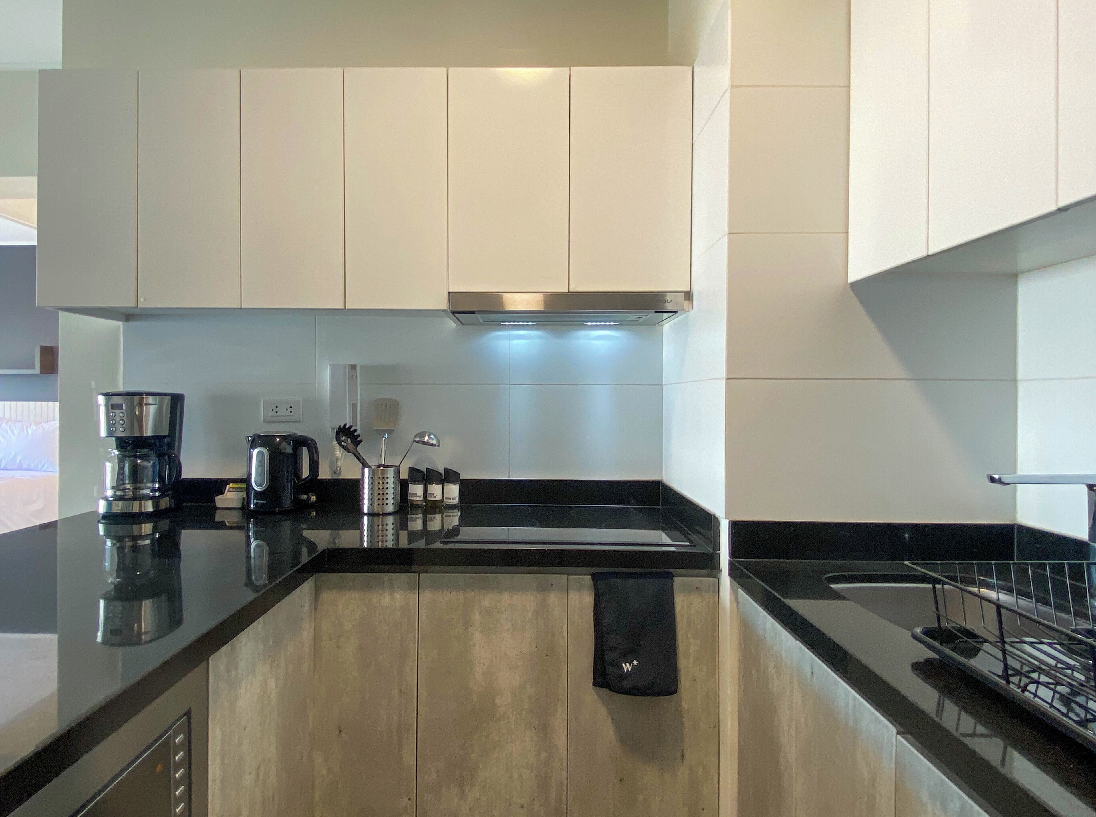 A modern kitchen with white cabinets, a black countertop, a coffee maker, a kettle, and a toaster.