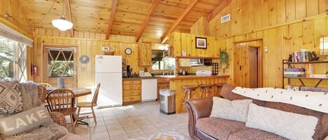 A cozy cabin interior with a wooden interior, a dining area, a kitchen, and a living room with a sofa and a coffee table.