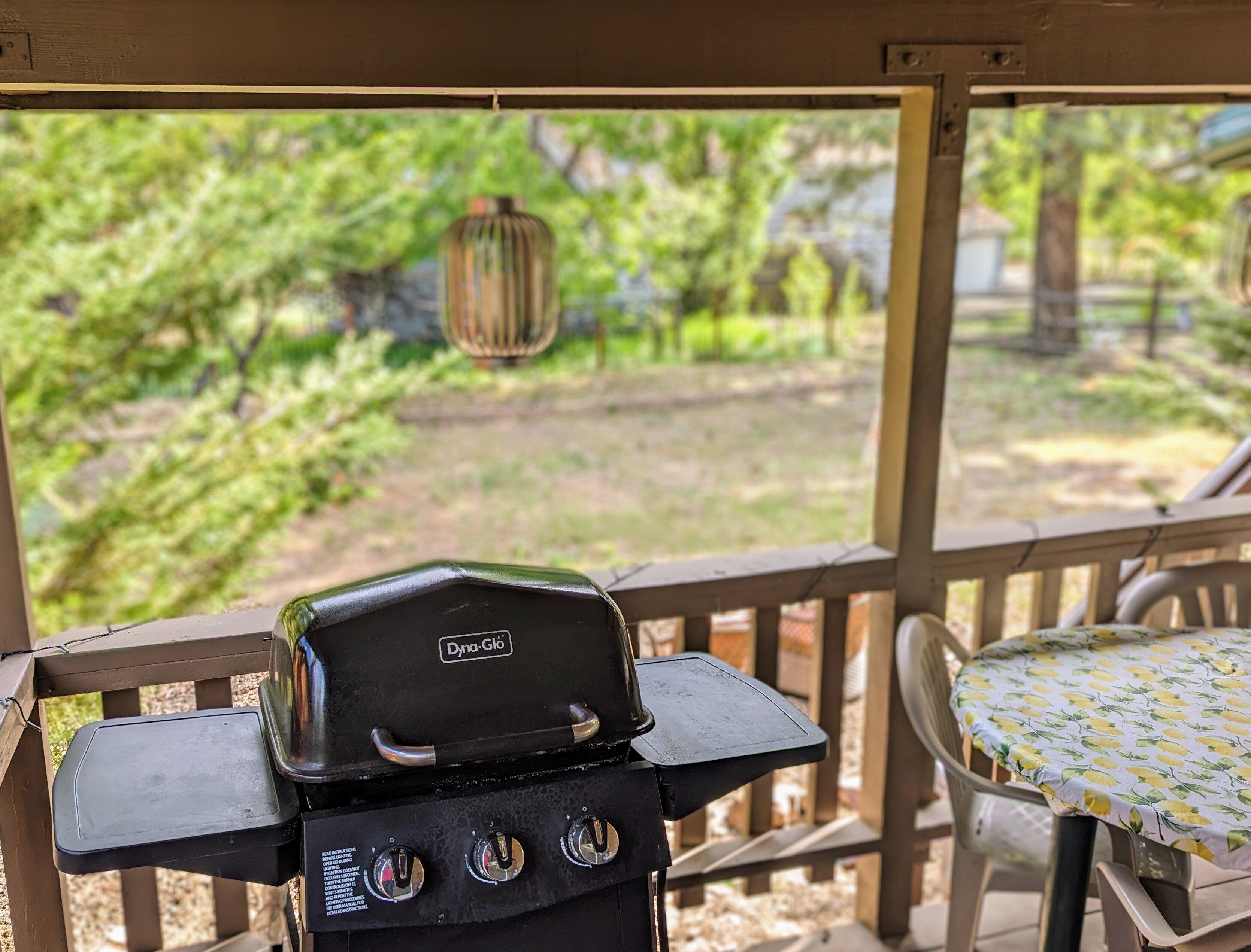 A barbecue grill with a view of a backyard with trees and a hanging lantern.