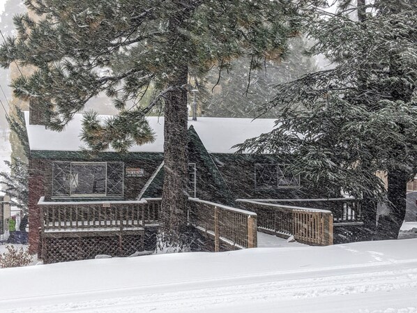Una cabaña nevada con terraza de madera y cerramiento de vidrio.
