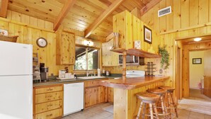 Una cocina tipo cabaña de madera con refrigerador, lavaplatos, microondas y taburetes de bar.