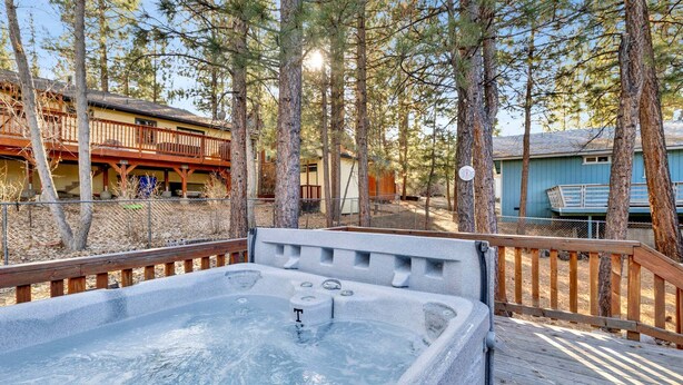 Un jacuzzi rodeado de terraza de madera y árboles, con un edificio al fondo.