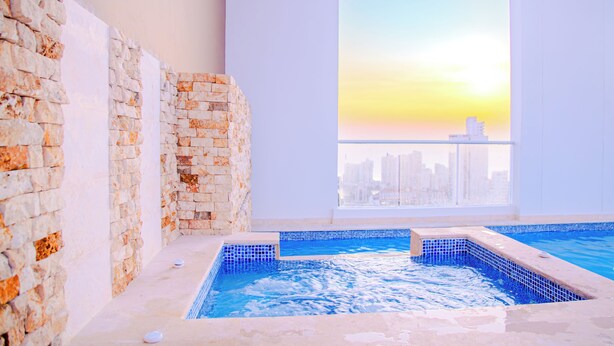 A modern indoor pool with a city skyline view, stone walls, and a clear sky. - Armonioso loft de 1 Hab en Ctg (Cartagena de Indias)
