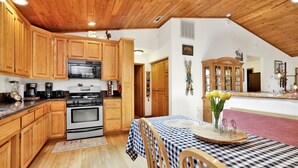 Una cucina con mobili in legno, un forno a microonde, un piano cottura e un'area pranzo con tovaglia a quadri e sedie.