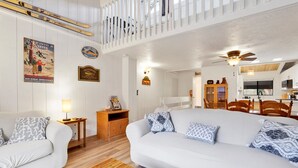 Een gezellige woonkamer met een witte bank, een houten salontafel en een eethoek met een houten tafel en stoelen.