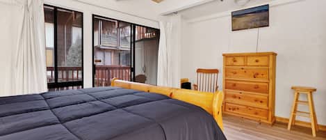 A bedroom with a large bed, wooden dresser, and a small stool.