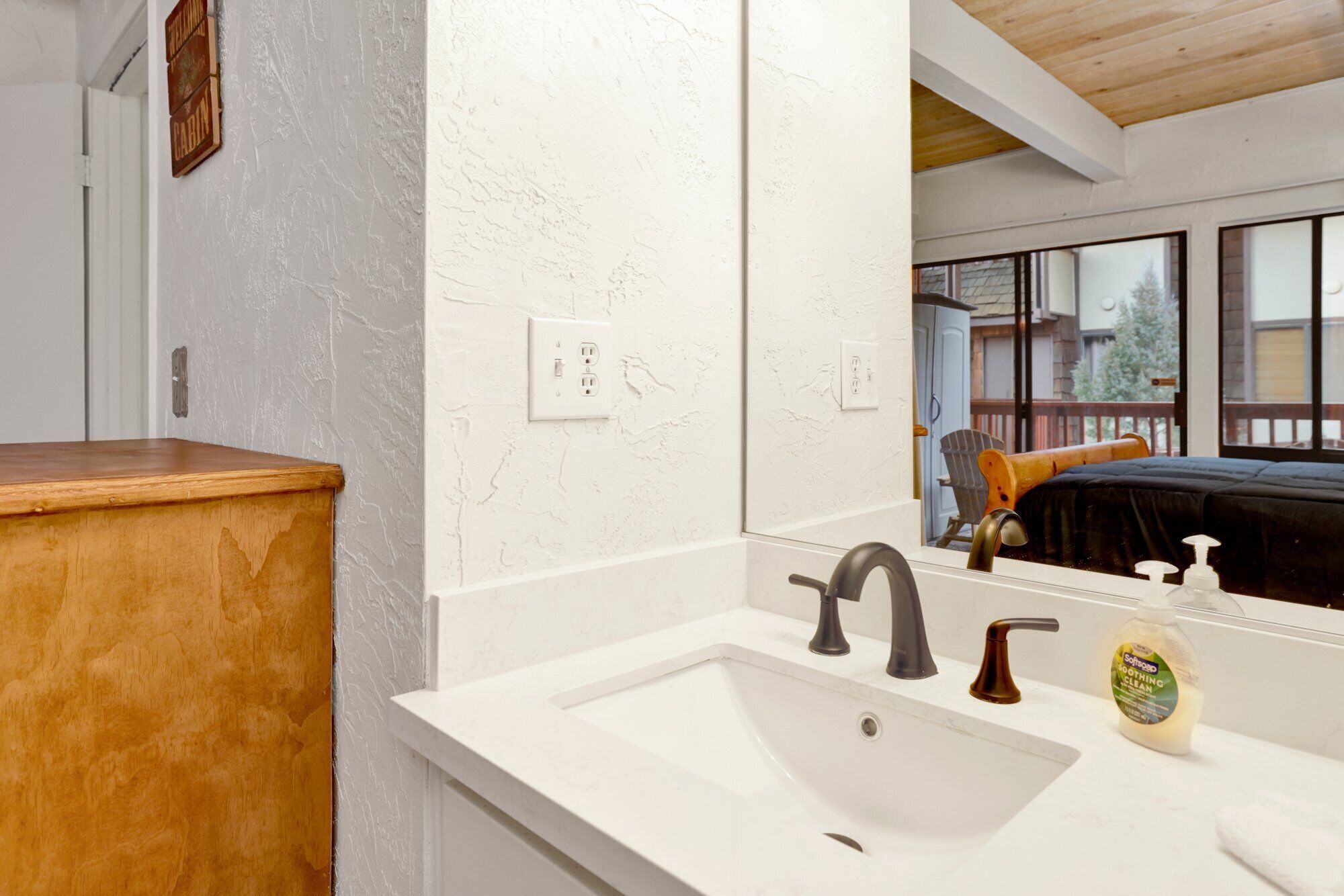 A bathroom with a white sink, two faucets, a soap dispenser, and a wooden counter.
