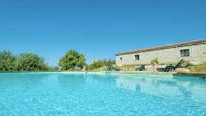 Une piscine d’un bleu éclatant, avec des chaises longues et un bâtiment en pierre en arrière-plan.