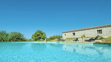 Ein klares, blaues Schwimmbecken mit Liegestühlen und einem dahinterliegenden Steinhaus.