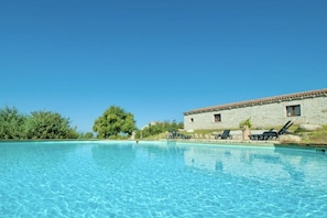 A clear blue pool with lounge chairs and a stone building in the background.