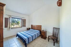 A bedroom with a bed, a chair, a nightstand, and a window.