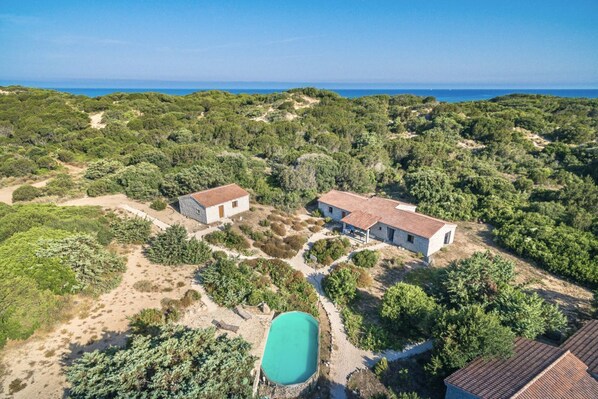An aerial view of a property with two buildings, a swimming pool, and a forested landscape.