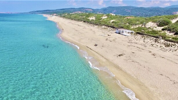 Una spiaggia con acque cristalline turchesi, una riva sabbiosa e alcune persone. Si nota una piccola struttura sulla spiaggia.