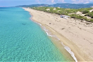 Uma praia com águas turquesa cristalinas, areia dourada e algumas pessoas. Há uma pequena construção na praia.