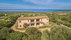 Un edificio a due piani con tetto in tegole, immerso nel verde e con vista sul mare.